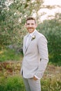 Groom in a suit stands near the olive tree