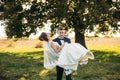 Groom took the bride in his arms and carried her to the field in background of big tree. Groom kisses bride