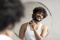 Grooming concept. Handsome young indian man looking at mirror and shaving beard with trimmer or electric shaver Royalty Free Stock Photo