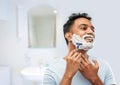 man shaving beard with razor blade in bathroom