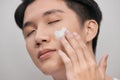 Grooming, skin care and people concept - smiling young indian man applying cream to face over white background