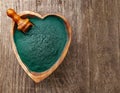 Ground Spirulina in bowl on wood background, top view on heart shape dish with superfood