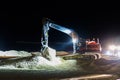 Ground worker working at nighttime in the dark with a digger machine moving the sand at the beach for maintenance