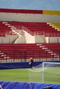 A groundskeeper tends to the lush green turf at a vibrant soccer stadium, adorned with colorful spectator seats