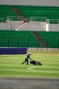 A groundskeeper tends to the lush green turf at a vibrant soccer stadium, adorned with colorful spectator seats