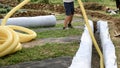 A worker carries a yellow perforated drainage pipe. Groundwater drainage works in the field