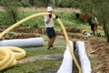 A worker carries a yellow perforated drainage pipe. Groundwater drainage works in the field