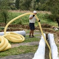 A worker carries a yellow perforated drainage pipe. Groundwater drainage works in the field