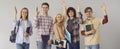 Group of active students in casual clothes raise their hands while standing on a gray background.