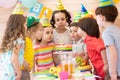 Group of adorable kids gathered around festival table. Children blow out candles on cake. Birthday party for Royalty Free Stock Photo