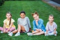 group of adorable schoolgirls sitting on green grass together and looking