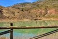 group of adult people with colorful backpack trekking on a path of sand and stones walking in single file next to a lake