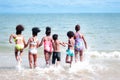 Group of African kids in swimsuit from behind have fun together on summer beach, boys and girls with black curly hair in line run Royalty Free Stock Photo