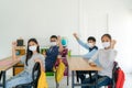 Group of Asian elementary school students wearing hygienic mask in classroom arm raised to be happy while back to school reopen Royalty Free Stock Photo