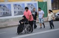 Group of Asian people walking down the street, young man pushing the wheelchair with an old disabled woman in black clothes