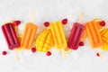 Assorted summer popsicles with ice and fruit, overhead on a white marble background