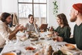 Group of attractive international friends sitting at the table full of food happily talking to each other. Young