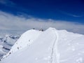 Back country skiers and mountain climbers near a high alpine summit cross with a narrow and exposed ridge leading towards them