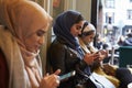 Group Of British Muslim Women Texting Outside Coffee Shop