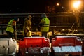 A group of builders repairs a bridge across the river at night under the light of lanterns in difficult winter conditions. Road