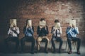 Group of business people sitting on chairs and covering their faces with paper against brick wall, Young people hiding their faces