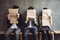 Group of business people sitting on chairs in office and looking at the camera, Young people hiding their faces behind resume