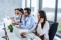 Group of call center workers with headsets using laptops in office. Royalty Free Stock Photo