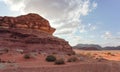 Group of camels grazing on small shrubs in orange red sand of Wadi Rum desert, tall rocky mountains background