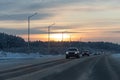 Group of cars with white lights is on the snowy road in winter on the orange sunset background Royalty Free Stock Photo