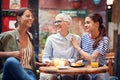 Group of females, two young and one elderly, sitting in outdoor cafe, talking, smiling, laughing