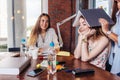 Group of cheerful college students doing homework together and goofing around while sitting at work table in classroom