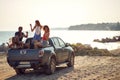 A group of cheerful friends is having a good time in the back of a car by the sea. Summer, sea, vacation, friendship