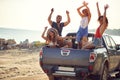 A group of cheerful handsome models is enjoying the music in the back of a car by the sea. Summer, sea, vacation, friendship