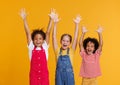 Group of cheerful happy multinational children shout with joy raising his hands up on yellow background Royalty Free Stock Photo