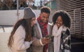 Group of cheerful multi-ethnic students looking at mobile phone and smiling, enjoying winter day outdoors Royalty Free Stock Photo