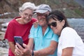 Group of cheerful senior Caucasian friends in leisure travel at sea sitting looking together at mobile phone. Two women and one Royalty Free Stock Photo