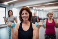 Group of cheerful seniors in gym doing exercise with dumbbells.