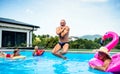 Group of cheerful seniors in swimming pool outdoors in backyard, jumping. Royalty Free Stock Photo