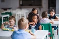 A group of cheerful small school kids in canteen, eating lunch.