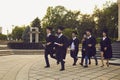 Group of cheerful university graduates walking with dimplomas in hands in park together