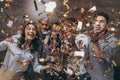 Group of cheerful young people standing together and celebrating with confetti