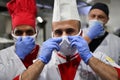 Group chefs standing together in the kitchen at restaurant wearing protective medical mask and gloves in coronavirus new normal