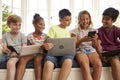 Group Of Children Sit On Window Seat And Use Technology