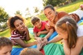 Group of children with teachers holding hands together on rainbow playground parachute in park. Summer camp activity Royalty Free Stock Photo
