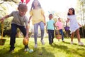 Group Of Children Wearing Bunny Ears Running To Pick Up Chocolate Egg On Easter Egg Hunt In Garden Royalty Free Stock Photo