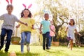 Group Of Children Wearing Bunny Ears Running To Pick Up Chocolate Egg On Easter Egg Hunt In Garden Royalty Free Stock Photo