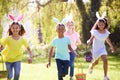 Group Of Children Wearing Bunny Ears Running To Pick Up Chocolate Egg On Easter Egg Hunt In Garden Royalty Free Stock Photo