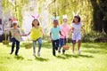 Group Of Children Wearing Bunny Ears Running To Pick Up Chocolate Egg On Easter Egg Hunt In Garden Royalty Free Stock Photo