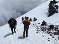 A group of climbers with backpacks and trekking poles stands and rests on a snowy trail