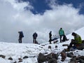 A group of climbers with backpacks and trekking poles stands and rests on a snowy trail